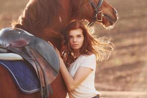jong vrouw omarmen haar paard in landbouw veld- Bij zonnig dag foto