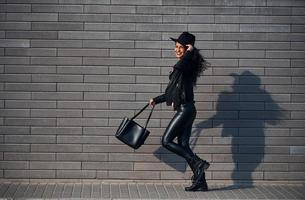 mooi brunette met gekruld haar- en in zwart kleren hebben wandelen buitenshuis in de buurt muur foto