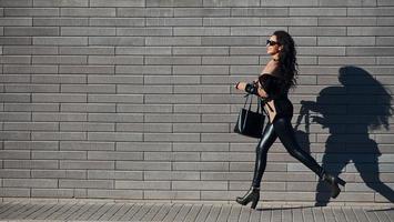 mooi brunette met gekruld haar- en in zwart kleren rennen buitenshuis in de buurt muur foto