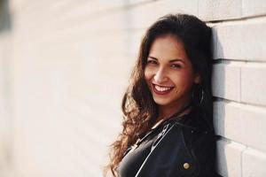 potrait van vrolijk brunette met gekruld haar- en in zwart kleren leunend Aan de muur foto