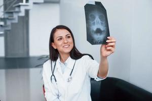 Holding röntgenfoto. jong verpleegster binnenshuis in modern kliniek. opvatting van gezondheidszorg foto