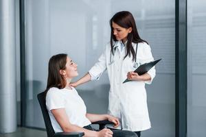 vriendelijk dokter luisteren naar de geduldig. jong vrouw hebben een bezoek met vrouw dokter in modern kliniek foto