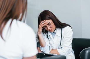 zittend en praten. jong vrouw hebben een bezoek met vrouw dokter in modern kliniek foto