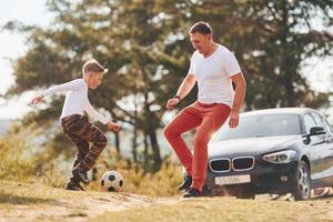 spelen voetbal. vader met zijn zoon uitgeven weekend samen buitenshuis in de buurt Woud Bij dag foto