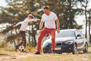 spelen voetbal. vader met zijn zoon uitgeven weekend samen buitenshuis in de buurt Woud Bij dag foto