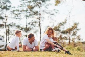 zittend en aan het liegen Aan de grond. gelukkig familie uitgeven weekend samen buitenshuis in de buurt de Woud. met dochter en zoon foto