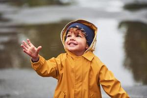 kind in geel waterbestendig mantel en laarzen spelen buitenshuis na de regen foto