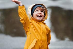 kind in geel waterbestendig mantel en laarzen spelen buitenshuis na de regen foto
