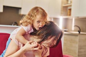 meisje wil ik hebben plezier. jong moeder met haar weinig dochter in gewoontjes kleren samen binnenshuis Bij huis foto