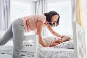 slaap tijd. jong moeder met haar weinig dochter in gewoontjes kleren samen binnenshuis Bij huis foto