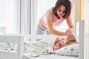 slaap tijd. jong moeder met haar weinig dochter in gewoontjes kleren samen binnenshuis Bij huis foto