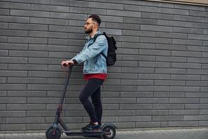 kant visie van knap jong vent in gewoontjes kleren dat rijden elektrisch schieter buitenshuis Bij zonnig dag foto