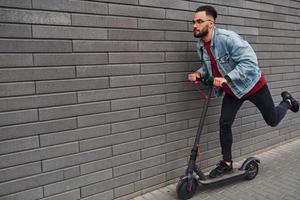 kant visie van knap jong vent in gewoontjes kleren dat rijden elektrisch schieter buitenshuis Bij zonnig dag foto