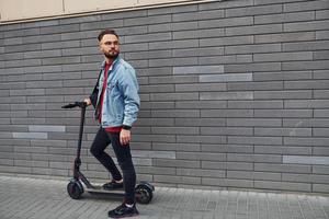 knap jong vent in gewoontjes kleren staand met elektrisch schieter buitenshuis Bij zonnig dag foto