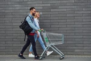 met boodschappen doen kar. jong elegant Mens met vrouw in gewoontjes kleren buitenshuis samen. opvatting van vriendschap of relaties foto