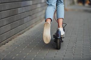 dichtbij omhoog visie van meisje in gewoontjes kleren dat rijden elektrisch schieter buitenshuis Bij zonnig dag foto