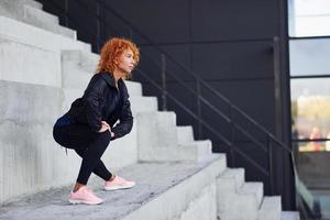 jong Europese roodharige vrouw in sportief kleren aan het doen opdrachten Aan trap buitenshuis foto
