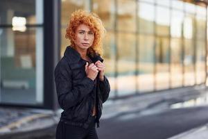 jong Europese roodharige vrouw in sportief kleren staand buitenshuis foto