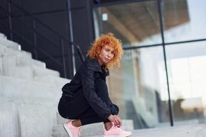 jong Europese roodharige vrouw in sportief kleren vervelend schoenen buitenshuis foto