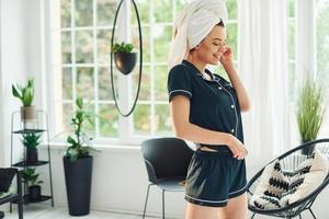 vrolijk jong vrouw in pyjama en wit handdoek Aan hoofd staand binnenshuis Bij dag foto