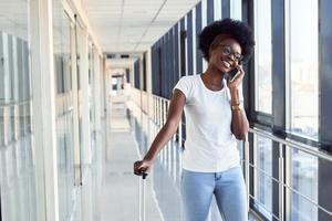 jong Afrikaanse Amerikaans vrouw passagier in gewoontjes kleren is in luchthaven met telefoon foto