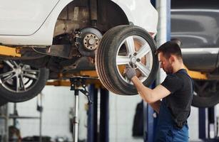 Mens in werk uniform veranderen auto wiel binnenshuis. opvatting van auto- onderhoud foto