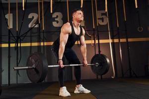 sterk Mens in sportief kleren hijs- barbell in de Sportschool foto