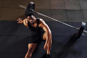 zittend Aan de vloer. sterk Afrikaanse Amerikaans Mens in sportief kleren hebben training dag in de Sportschool foto