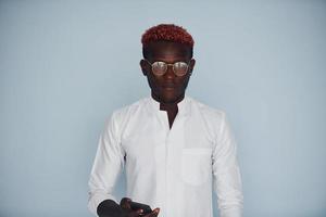 jong Afrikaanse Amerikaans Mens in wit formeel kleren pratend door de telefoon tegen muur binnenshuis foto