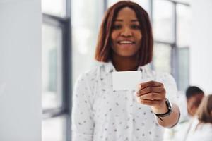 vrouw houdt bedrijf kaart kaart. groep van Afrikaanse Amerikaans mensen werken in kantoor samen foto