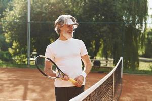 senior modern elegant Mens met racket buitenshuis Aan tennis rechtbank Bij dag foto