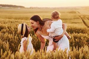 vrolijk familie van moeder, weinig zoon en dochter uitgeven vrij tijd Aan de veld- Bij zonnig dag tijd van zomer foto