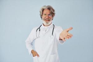 professioneel positief dokter. senior elegant modern Mens met grijs haar- en baard binnenshuis foto