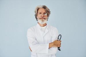 dokter in wit jas tegen muur. senior elegant modern Mens met grijs haar- en baard binnenshuis foto