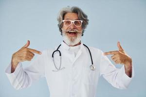 professioneel positief dokter. senior elegant modern Mens met grijs haar- en baard binnenshuis foto