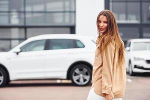 wandelingen dichtbij auto. modieus mooi jong vrouw en haar modern auto- foto