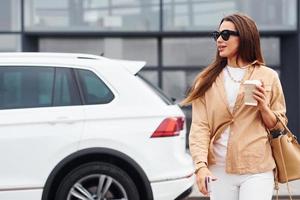 buitenshuis tegen modern gebouw. modieus mooi jong vrouw en haar modern auto- foto