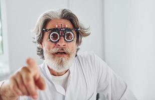 mooi hoor gelaats uitdrukkingen. senior Mens met grijs haar- en baard is in oogheelkunde kliniek foto