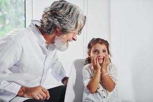 werken met weinig bezoeker. senior mannetje dokter met grijs haar- en baard in wit jas is binnenshuis in kliniek foto