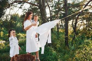 huisvrouw drogen kleren. jong moeder met haar weinig dochter en zoon is buitenshuis in de Woud. mooi zonneschijn foto