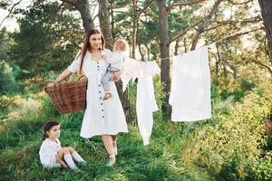 huisvrouw drogen kleren. jong moeder met haar weinig dochter en zoon is buitenshuis in de Woud. mooi zonneschijn foto