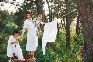 huisvrouw drogen kleren. jong moeder met haar weinig dochter en zoon is buitenshuis in de Woud. mooi zonneschijn foto