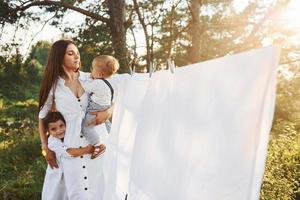 huisvrouw drogen kleren. jong moeder met haar weinig dochter en zoon is buitenshuis in de Woud. mooi zonneschijn foto