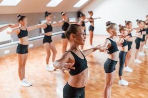 staand in de rij. groep van vrouw kinderen beoefenen atletisch opdrachten samen binnenshuis foto