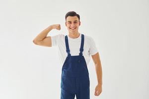 shows biceps. klaar naar werk. mannetje arbeider in blauw uniform staand binnen van studio tegen wit achtergrond foto