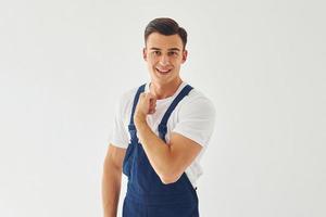 shows biceps. klaar naar werk. mannetje arbeider in blauw uniform staand binnen van studio tegen wit achtergrond foto