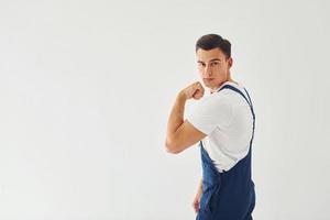 shows biceps. klaar naar werk. mannetje arbeider in blauw uniform staand binnen van studio tegen wit achtergrond foto