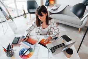 met laptop Aan de tafel. jong vrouw freelance arbeider is binnenshuis in huis Bij dag foto