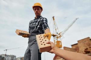 duurt steen van andere jongen. bouw arbeider in uniform en veiligheid uitrusting hebben baan Aan gebouw foto