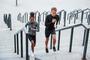 rennen Aan tribunes. Europese Mens en Afrikaanse Amerikaans vrouw in sportief kleren hebben training samen foto